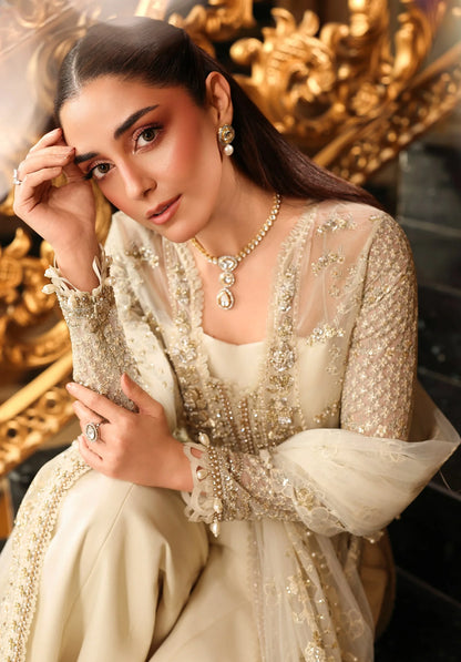 Woman in a cream-colored embroidered outfit with gold jewelry against a decorative gold background