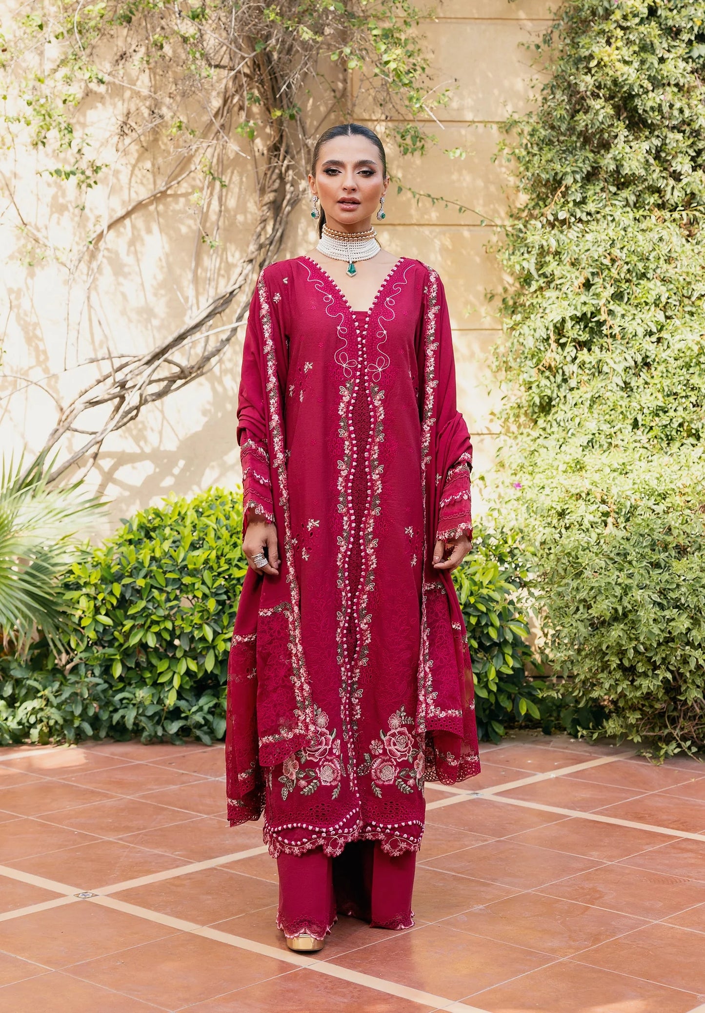 Woman wearing a red embroidered outfit standing outdoors with greenery in the background