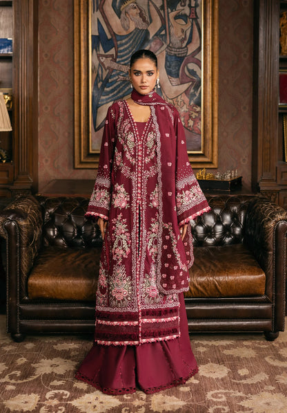 Woman in a burgundy embroidered dress standing in an elegant room with leather furniture and a decorative wall.