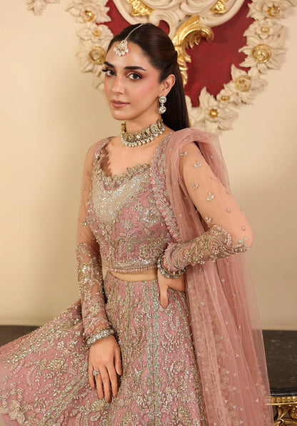 Woman in traditional pink and gold embroidered outfit with jewelry, sitting against a decorative background.