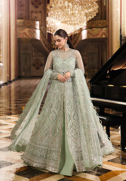 Woman in a light green embroidered traditional outfit standing in an elegant interior setting with a chandelier and piano.