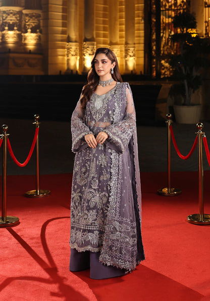 Woman in a purple embroidered outfit on a red carpet with a decorated background