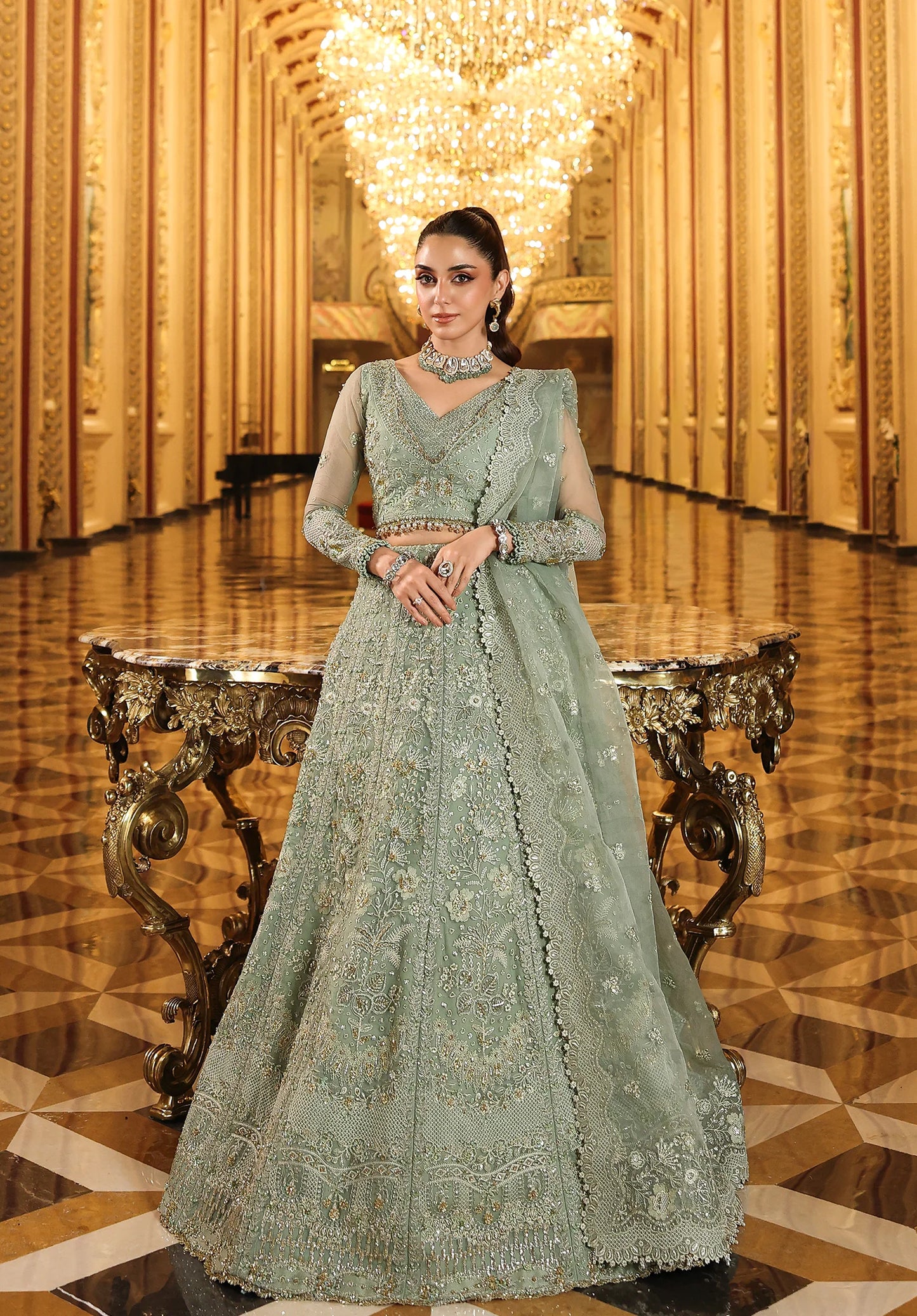 Woman in a light green embroidered traditional outfit standing in an opulent room with chandelier with with Elaf Stardom Handwork.