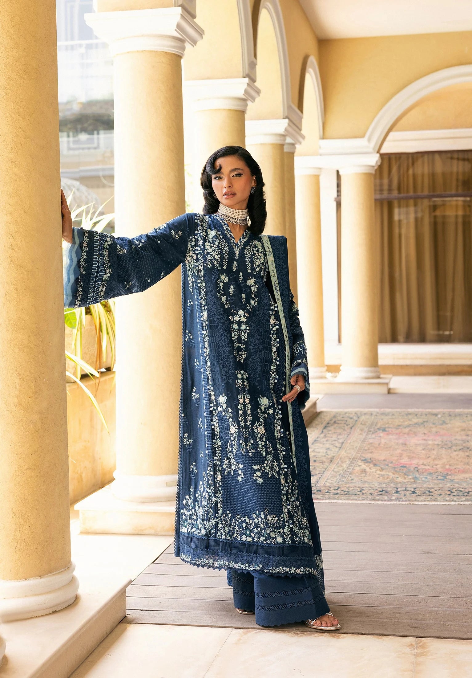 Woman in a blue embroidered traditional outfit standing in an architectural setting with ELAF LUXURY WINTER