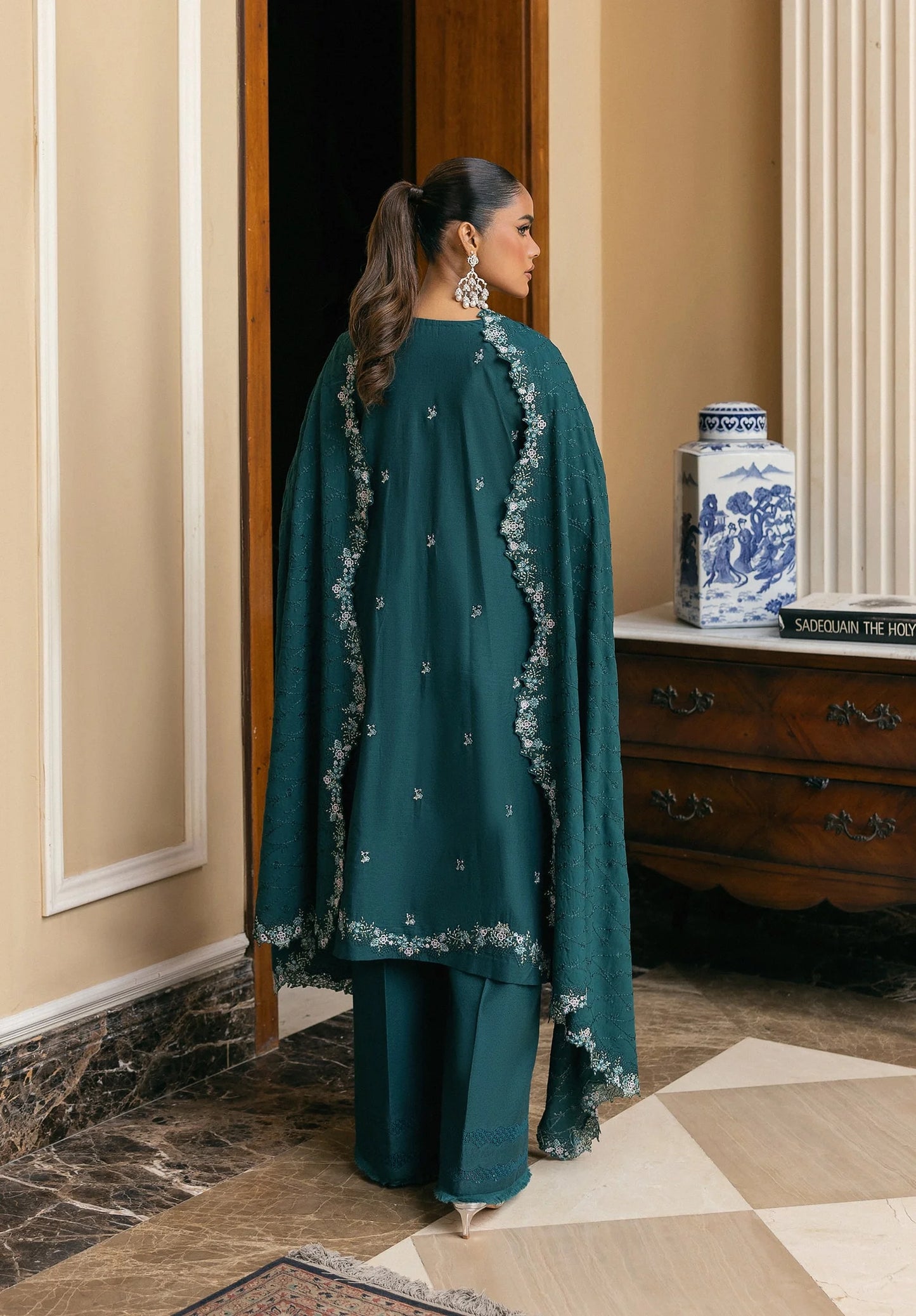 Woman in a teal traditional outfit standing in a room with decorative elements.
