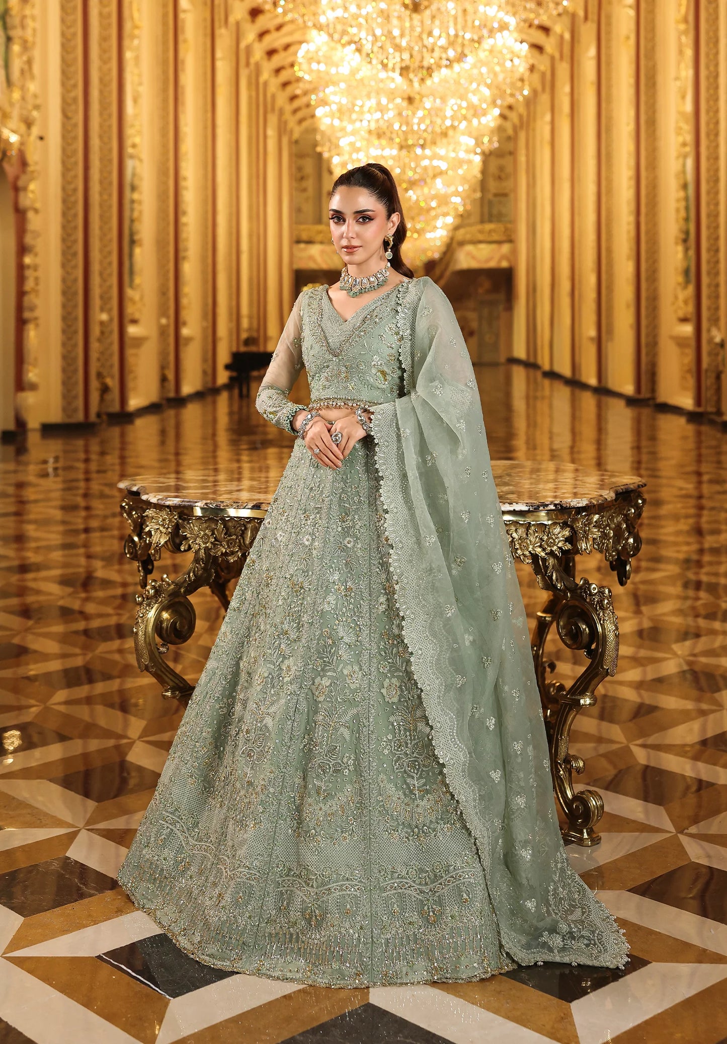 Woman in a light green embroidered traditional outfit standing in an opulent room with gold decor in with Elaf Stardom Handwork