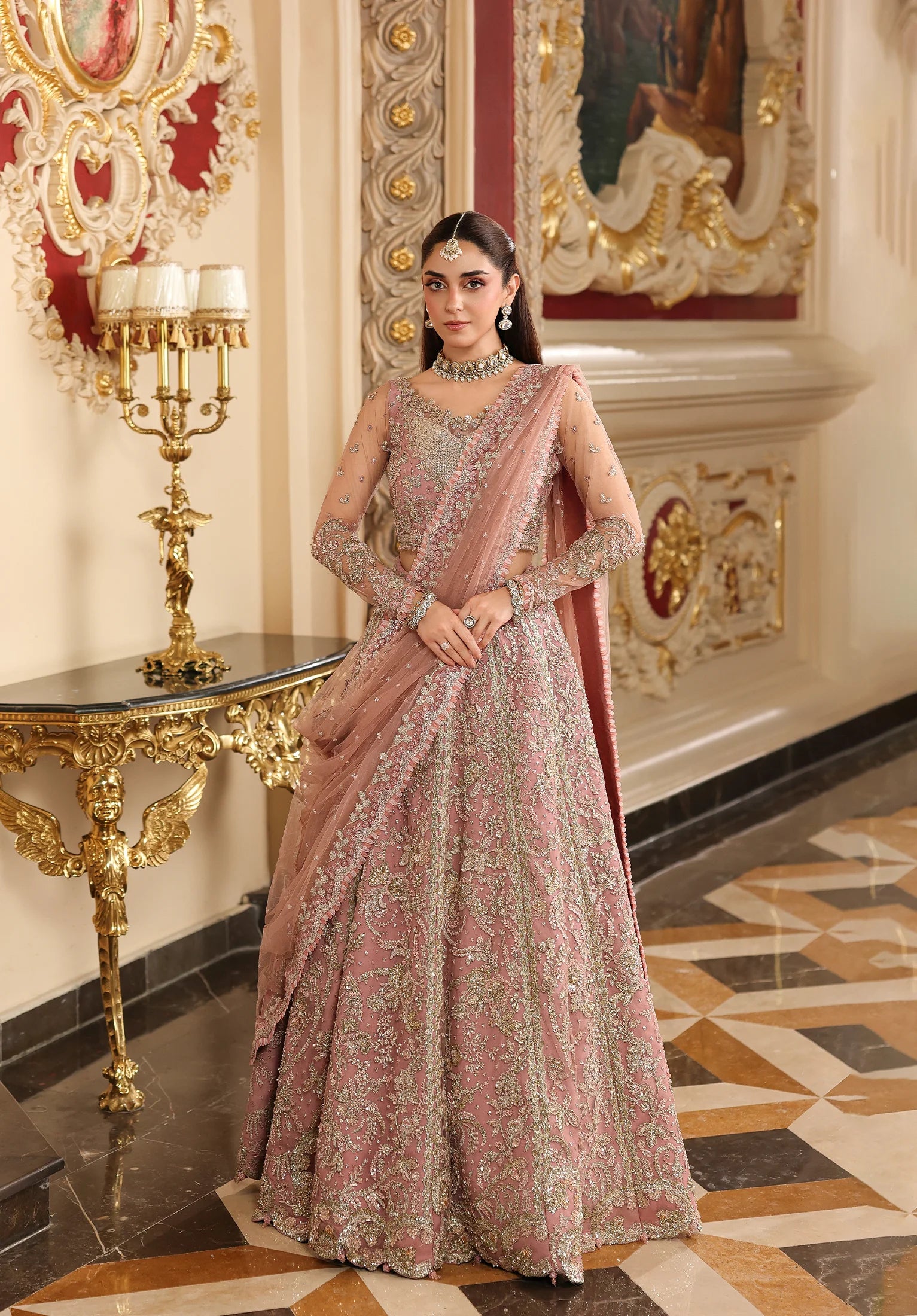 Woman in a traditional pink and gold embroidered outfit standing in an ornate room with Elaf Stardom Handwork